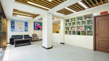 A lobby with a reception desk, a sofa, a coffee table, and a shelving unit with plants.