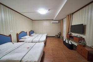 A hotel room with three beds, a flat-screen TV, a wooden dresser, and an air conditioning unit.