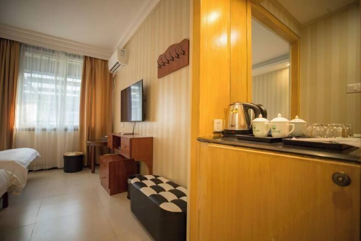 A hotel room with a bed, a desk, a chair, a small table with tea cups, a kettle, and a mirror.