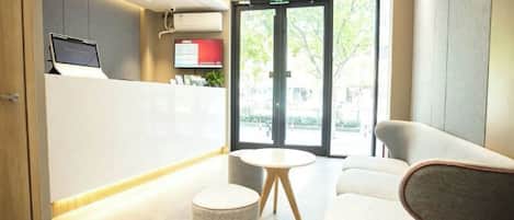 A reception area with a reception desk, a seating area with a round table and chairs, and a large glass door leading outside.