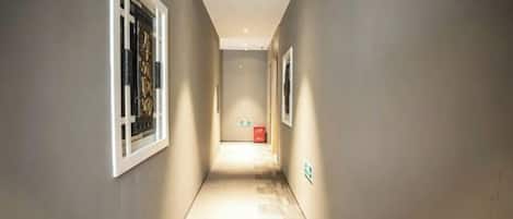 A narrow hallway with a carpeted floor, white-framed windows, and a red emergency exit sign.