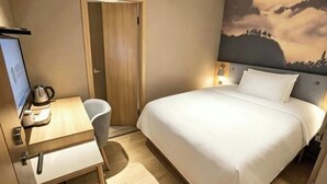 Ein Hotelzimmer mit Bett, Schreibtisch mit Computer, Stuhl, Tür und einem Bild an der Wand.