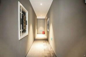 Un pasillo estrecho con piso alfombrado, ventanas con marco blanco y un letrero rojo de salida de emergencia.