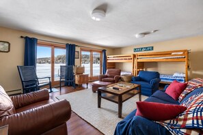 Una sala de estar acogedora con un sofá, sillas, una mesa de centro y una cama litera con el letrero 'LAKE LIFE'.