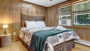 A bedroom with wooden paneling, a bed with patterned bedding, a ceiling fan, and a window with blinds.