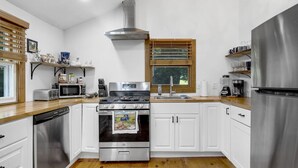 A modern kitchen with white cabinets, stainless steel appliances, a built-in oven, and a window with blinds.