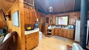 Eine gemütliche Küchenzeile im Blockhausstil mit Holzausstattung, einem Essbereich mit Korbstuhl und einem großen Fenster.