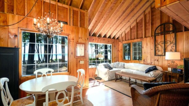 Ein Holzblockhaus-Interieur mit Esstisch, Stühlen, einer Couch und einem Fernseher.