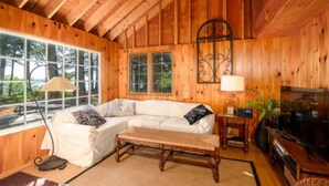 Ein gemütliches Blockhauss-Interieur mit Holzbalkendecke, einem Ecksofa, einer Bank, einer Lampe und einem Fernseher.