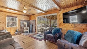 A cozy cabin interior with a fireplace, leather sofas, and a TV mounted on the wall. - Peaceful Escape | Dock Option + Fire pit | Winni (Moultonborough)