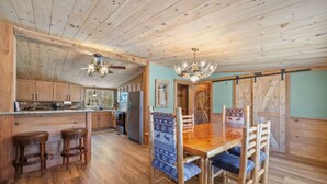 A rustic kitchen with wooden cabinets, a central island, and a dining area with a wooden table and chairs. - Peaceful Escape | Dock Option + Fire pit | Winni (Moultonborough)