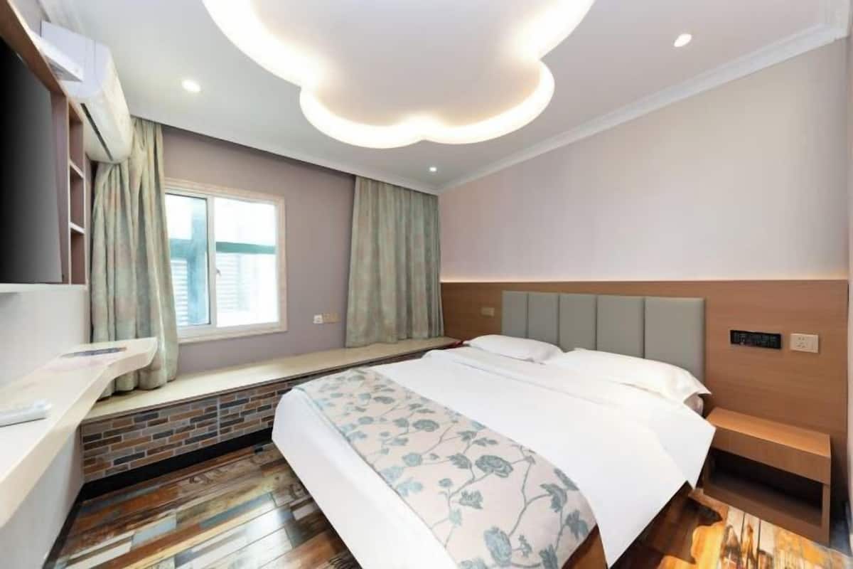 A modern hotel room with a bed, a built-in bench, a window with curtains, and a unique ceiling design.