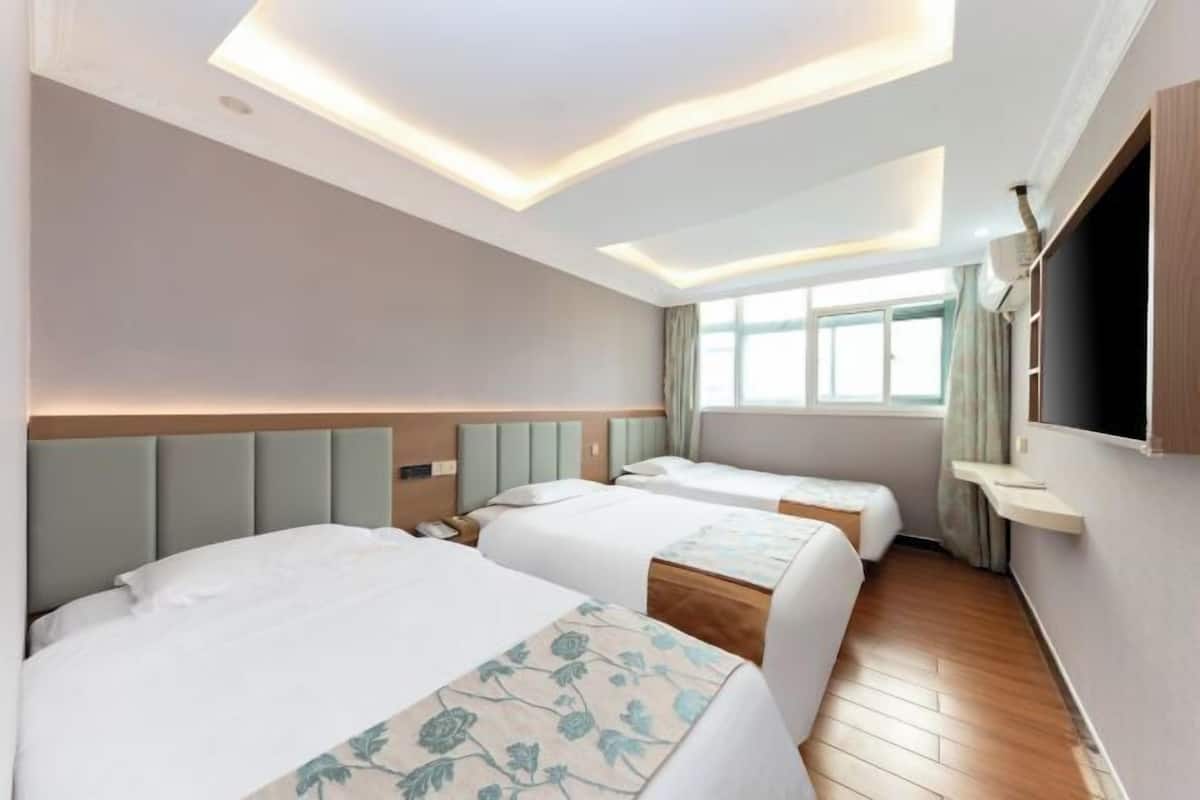A hotel room with two beds, a TV, a window with curtains, and a wooden floor.
