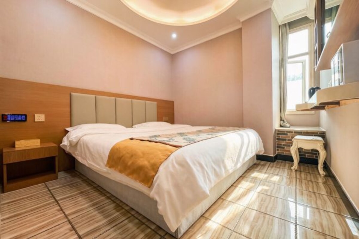 A bedroom with a bed, bedside table, nightstand, and a window.