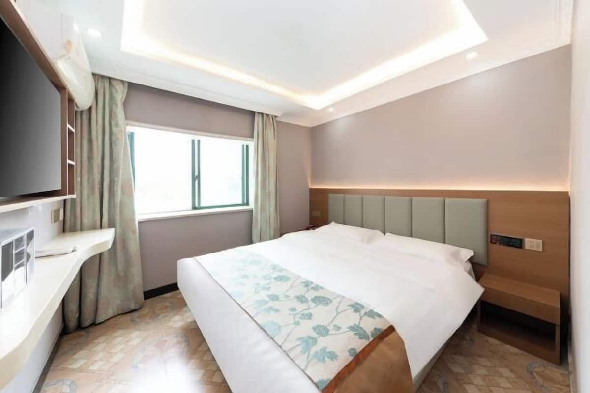 A hotel room with a bed, a TV, a window, and a ceiling light fixture.