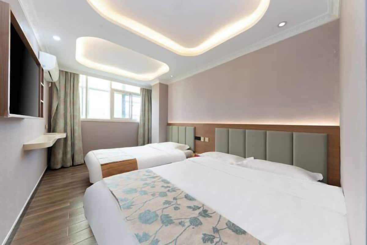 A hotel room with two beds, a TV, a window with curtains, and a modern ceiling design.
