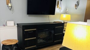 A modern living room with a flat-screen TV mounted on the wall, a black entertainment unit, a wooden coffee table, and a glass coffee table. - The Suite at North Shore Long Island, Prime Location, Unique and sophisticated (Smithtown)