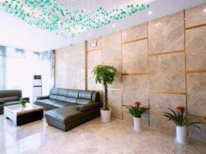 A modern lobby with a leather sofa, a coffee table, potted plants, and a marble wall with geometric patterns. - Longqiao Hotel (Yichang Yiting Three Gorges Airport) (Yichang)