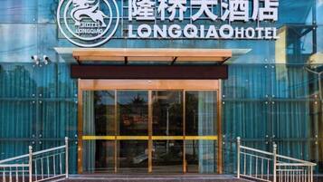 The entrance to the Longqiao Hotel with a glass facade and metal railings.