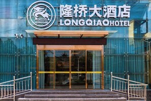 The entrance to the Longqiao Hotel with a glass facade and metal railings.