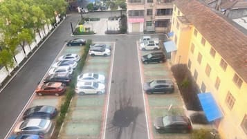 A parking lot with multiple rows of parked cars, a building with a tiled roof, and a tree-lined street.