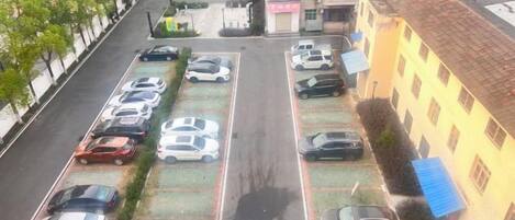A parking lot with multiple rows of parked cars, a building with a tiled roof, and a tree-lined street.