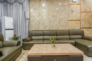 A modern living room with a sectional sofa, a marble coffee table, and a white appliance in the background.