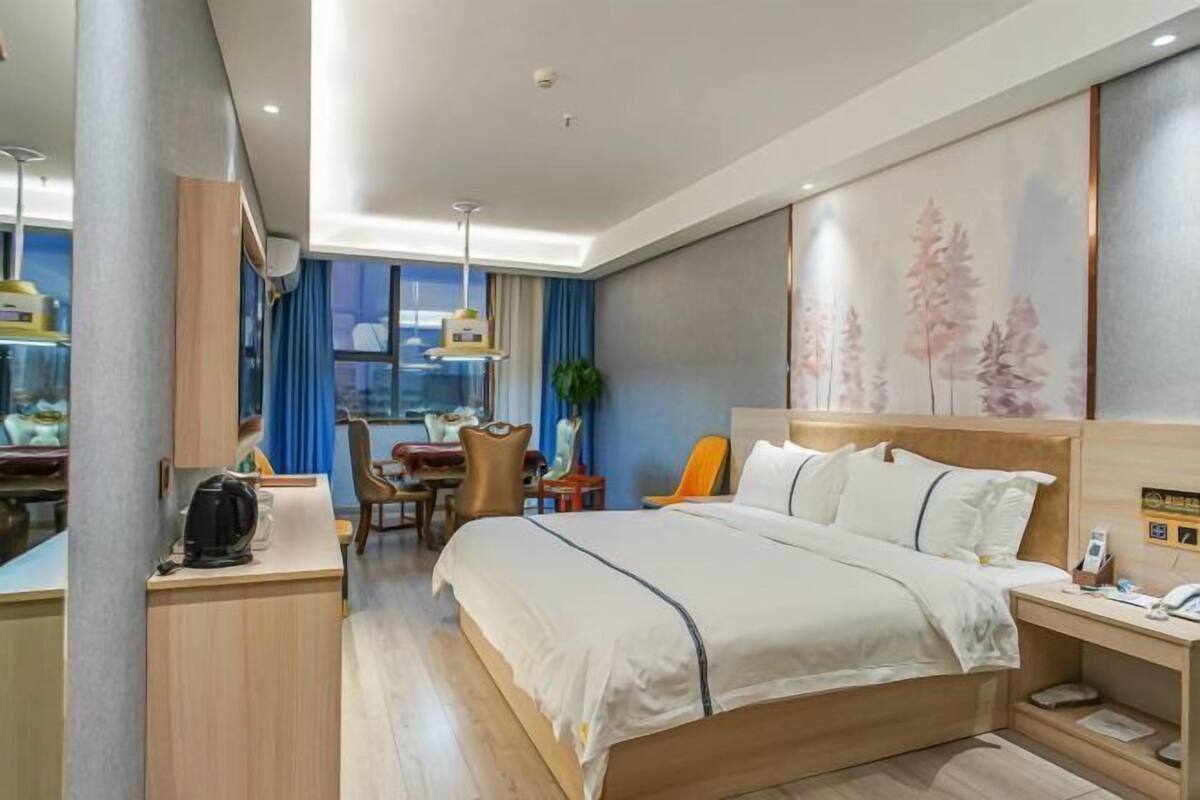 A hotel room with a bed, desk, chair, and a view of the city.