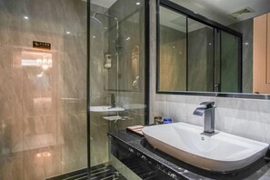 A modern bathroom with a glass-enclosed shower, a white sink with a single faucet, and a large mirror above the sink.
