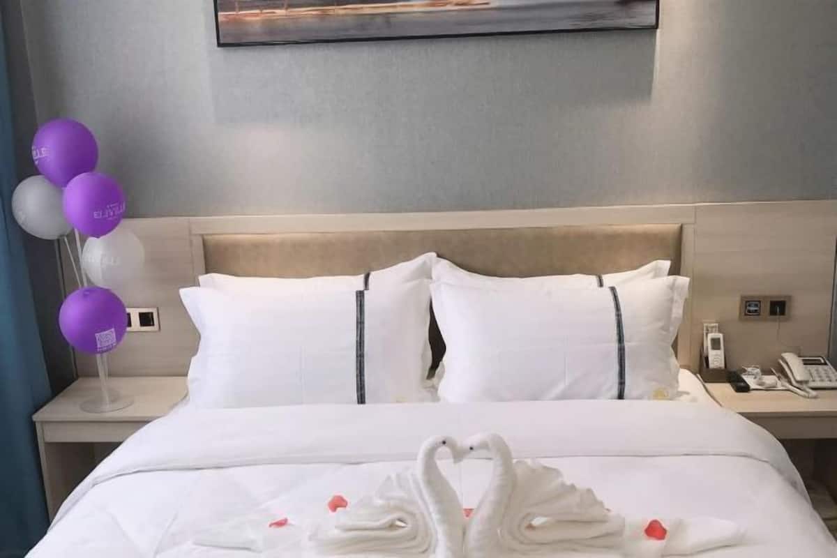 A hotel room with a bed, pillows, a bedside table with a phone, and a wall-mounted artwork.