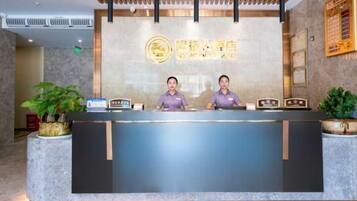 A reception desk with two staff members, a reception area, and a wall-mounted sign.
