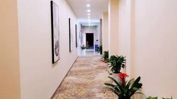 A hallway with framed pictures on the walls, potted plants, and a patterned floor.