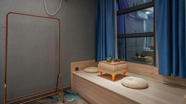 Une pièce avec un banc en bois, un petit tabouret en osier et une fenêtre ornée de rideaux bleus.