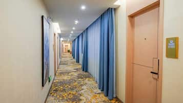A hotel corridor with a patterned carpet, blue curtains, and a door with a sign.