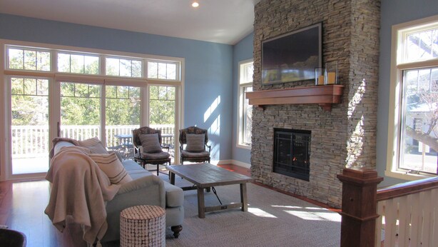 A spacious living room with a stone fireplace, large windows, and a ceiling fan. - Fish Creek Beautiful Downtown Condo Sleeps 8 (Fish Creek)