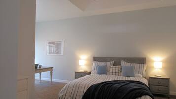 A bedroom with a bed, two bedside tables with lamps, a nightstand, a desk, and a ceiling fan.