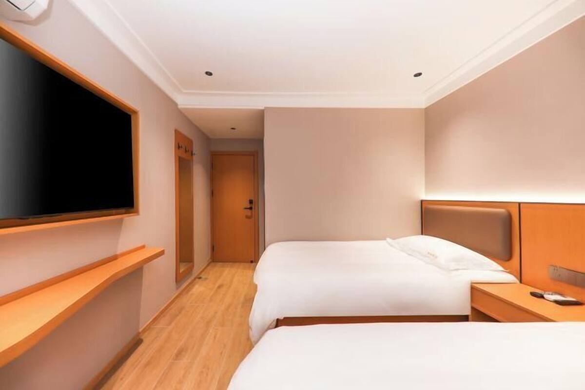 A hotel room with two beds, a TV mounted on the wall, and a wooden floor.