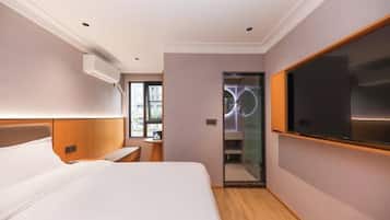 Een hotelkamer met een bed, een televisie, een spiegel en een badkamer met een glazen deur.