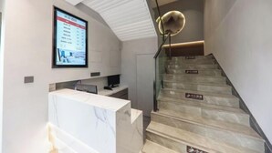 A modern hotel lobby with a reception desk, a digital information board, and a staircase with directional signs. - Miduo Hotel (Shanghai)