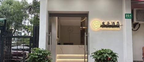 A hotel entrance with a reception desk, a staircase leading inside, and a sign indicating the hotel's name.