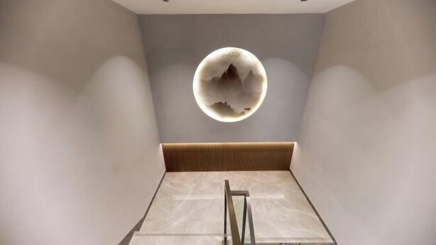 A modern interior with a unique circular light fixture on the wall, a wooden bench, and a glass railing. - Miduo Hotel (Shanghai)