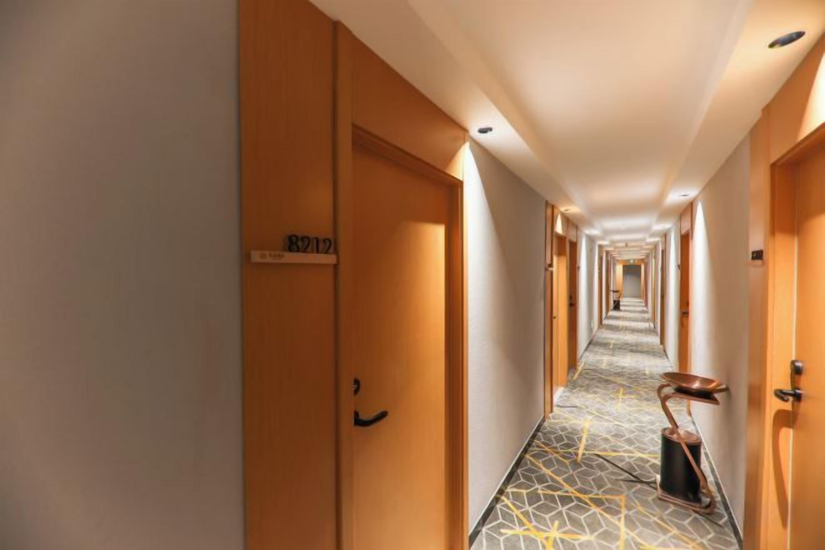 A hotel corridor with wooden doors, a number sign, and a patterned floor.