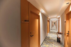 A hotel corridor with wooden doors, a number sign, and a patterned floor.