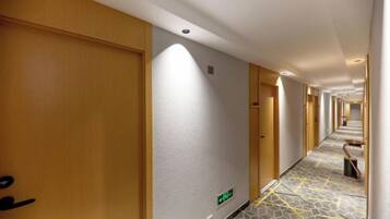 Un pasillo de hotel con puertas de madera, alfombra estampada y un largo recorrido hacia la recepción.