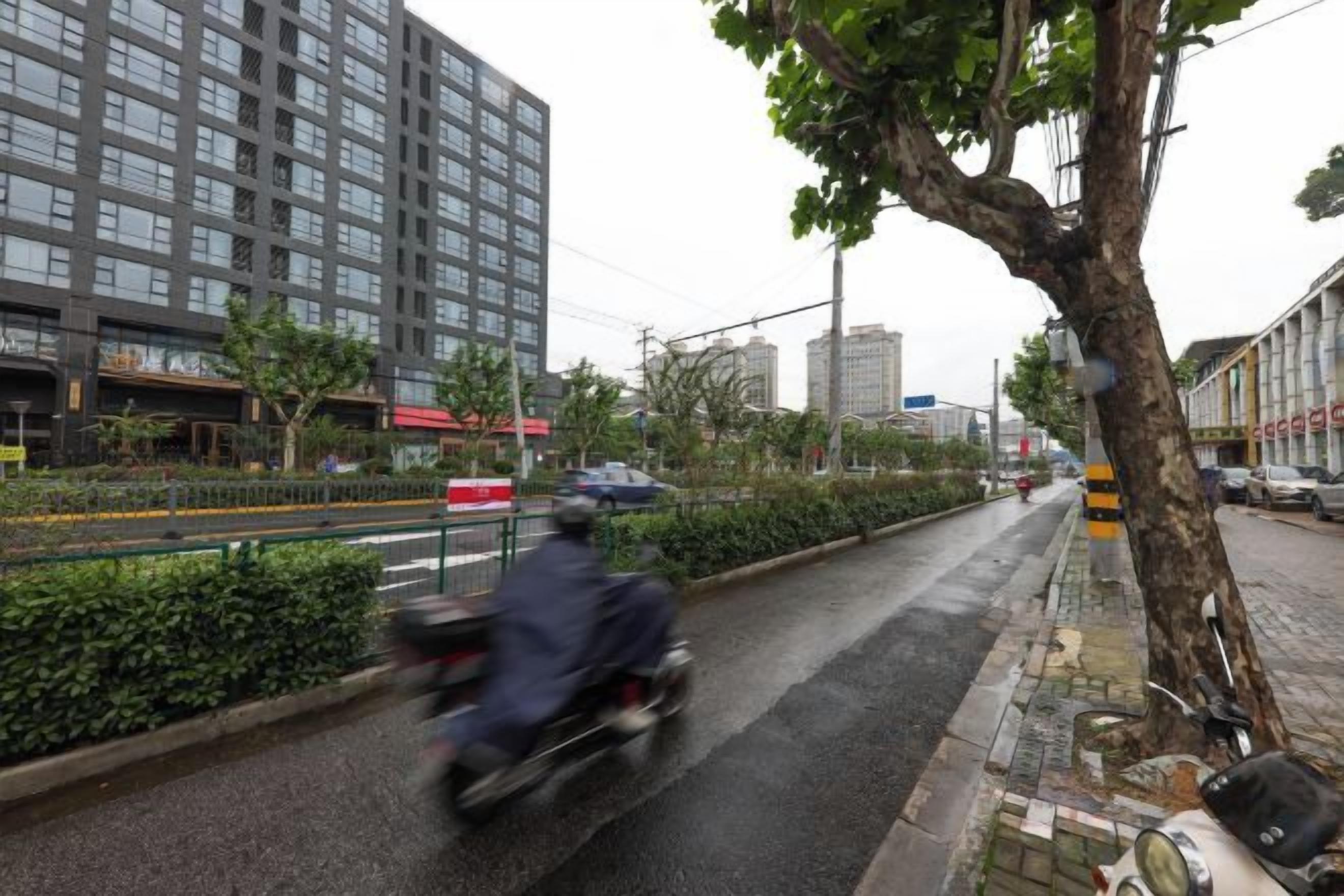 A street scene with a building, a tree, and a motorbike.