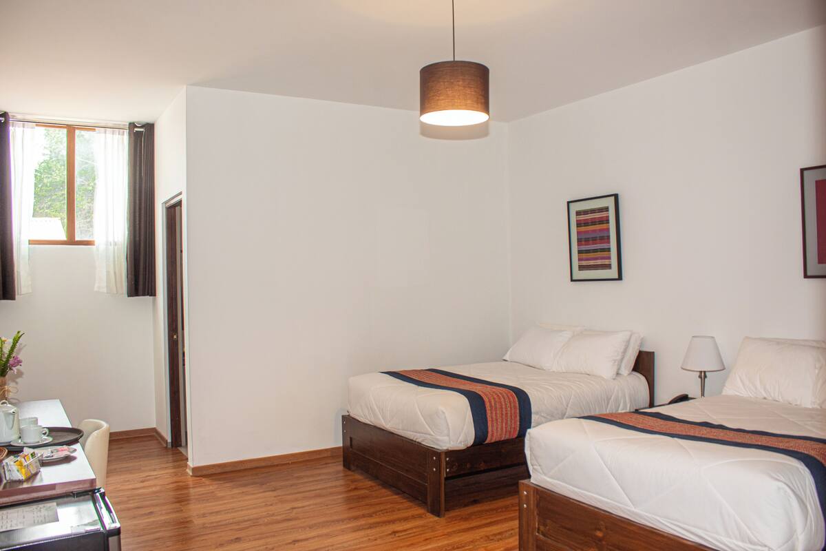 Een hotelkamer met twee bedden, een houten vloer, een hanglamp en een raam met gordijnen.