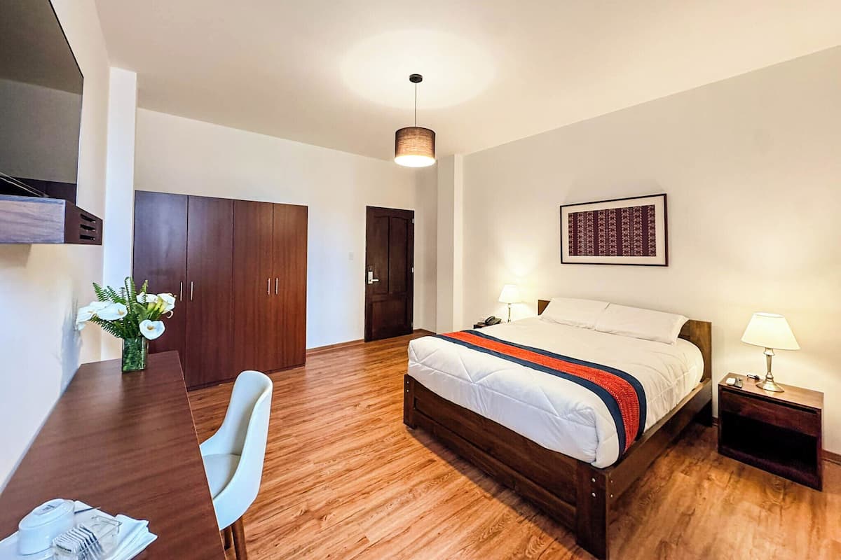 Een hotelkamer met een bed, een bureau, een stoel, een kledingkast en een lijst aan de muur.