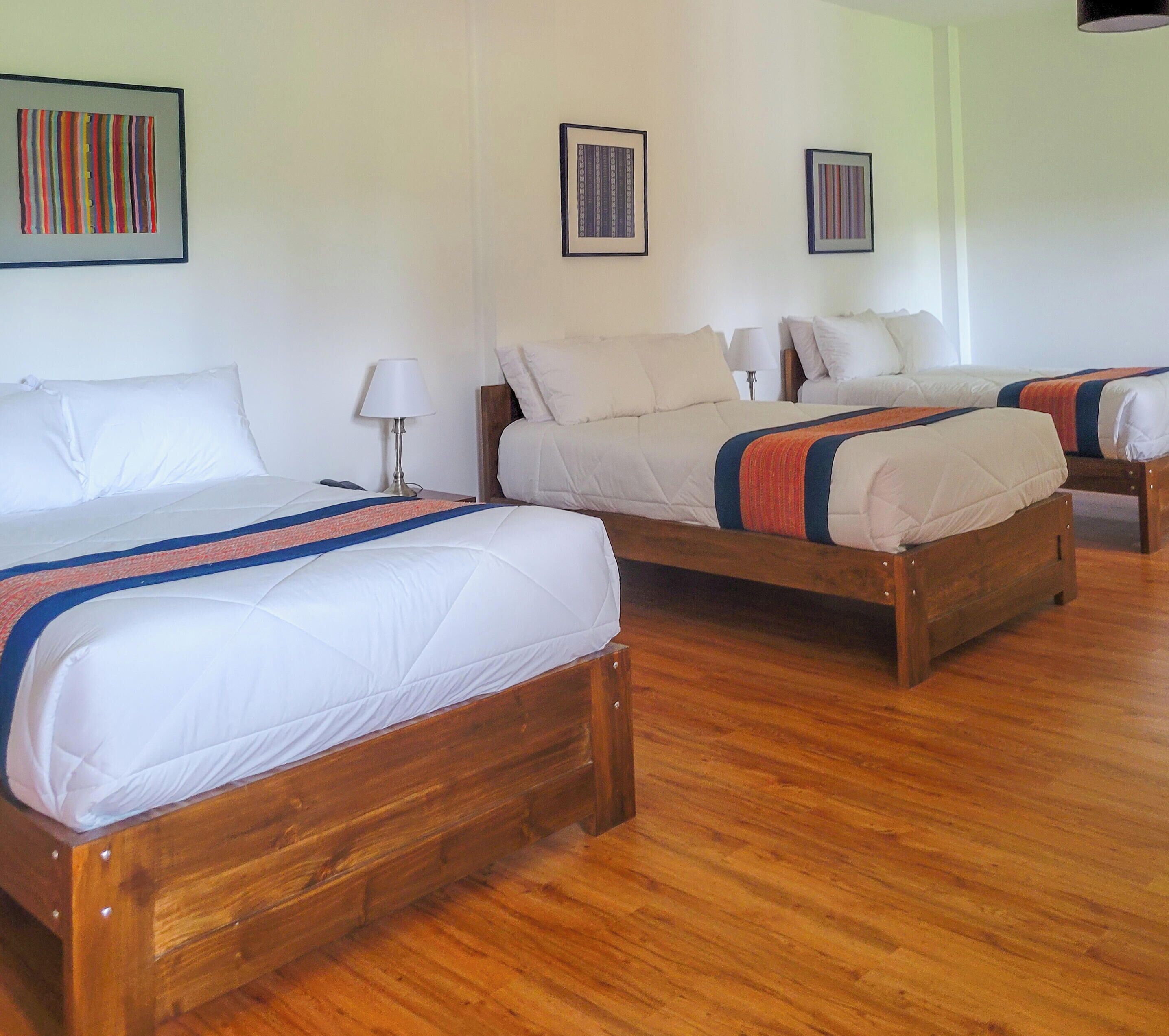 Una habitación de hotel con tres camas de madera, ropa de cama blanca y suelo de madera.