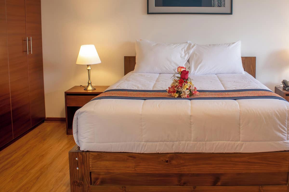 Een hotelkamer met een houten bed, wit beddengoed, twee bedlampen, een telefoon en een ingelijste foto aan de muur.