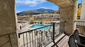 Un balcon agrémenté d’une arche en pierre, donnant sur une piscine et un parking rempli de voitures.